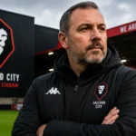 Peter Cklamovski Salford City manager poses with arms crossed at the Peninsula Stadium