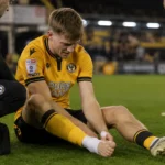James Crole ankle injury sees Newport striker sit on the pitch clutching his bare foot as a member of staff attends to him during a match at Rodney Parade